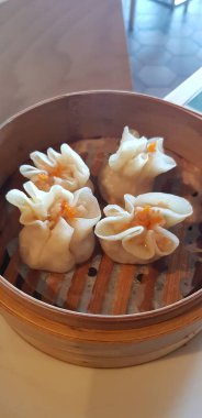 Güzelce hazırlanmış bir masada duran bambu buharlı buharlı tencereye dikkatlice yerleştirilmiş lezzetli bir Dim Sum görüntüsü.