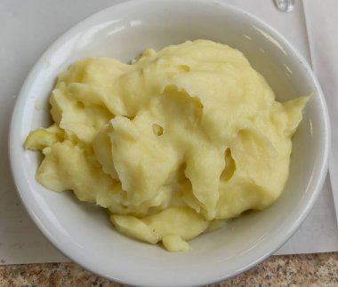 Herkesin keyif alması için ahşap bir masaya yerleştirilmiş kremalı patates püresi dolu beyaz bir kase var.