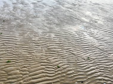 Bu güzel kumlu bir sahilin yakın görüntüsü. Dalgalar yavaşça kıyıya vuruyor. Huzurlu bir atmosfer manzarası yaratıyor.