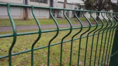 Bu video yeşil tel çitli sakin bir parkı, bir binaya yakın çekimleri, yemyeşil otları ve canlı ağaçları gösteriyor.