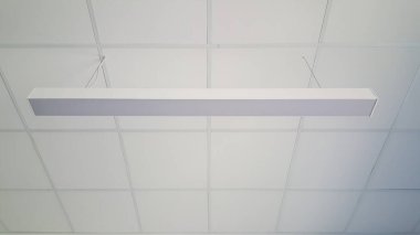 Odanın tavanından sarkan uzun floresan beyaz bir ışık mekanı aydınlatıyor ve parlak bir atmosfer yaratıyor.