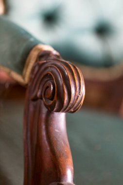 Bu çok güzel hazırlanmış ahşap bir sandalyenin detaylı bir yakın çekimi. Arka planda rahat yeşil bir kanepe var.