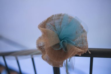 Çuval bezi ve mavi tülden yapılmış güzel bir çiçek bir korkuluğa asılır ve çevreye büyüleyici bir dokunuş ekler.