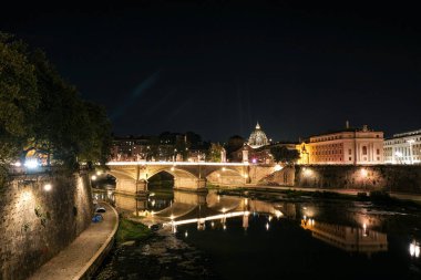 Roma, İtalya 'da Tiber Nehri, Ponte Sant' Angelo ve St. Peter 's Dome' un yer aldığı bir gece manzarası. Aydınlatılmış şehir manzarası resim gibi bir manzara yaratıyor. Seyahat ve şehir gece temaları için ideal