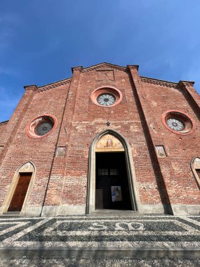 İtalya, Pinarolo 'da tarihi bir kilise cephesi manzarası. Resim tuğla, gül rengi pencere ve mimari ayrıntıları gösteriyor. Mimarlık, seyahat ve İtalyan kasaba temalarına uygundur..