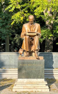 A full shot of the statue of Indro Montanelli, an Italian journalist and writer, seated on a bench in a park, holding a book. clipart