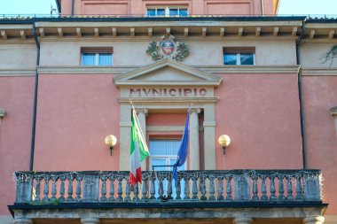 Önünde İtalyan ve Avrupa Birliği bayrakları sallanan taştan bir balkonlu bir İtalyan belediye binası veya belediye binasının ön çekimi.