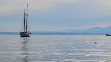 Gün batımında, İtalya, Garda Gölü 'nün sakin sularında süzülen bir yelkenlinin sakin görüntüsü. Güneşin altın ışığı su ve dağlara yansıyor..