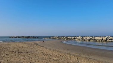 Adriyatik Denizi boyunca bir kış günü Rimini 'de boş bir plaj. Kaya dalgaları, berrak ve soğuk bir gökyüzünün altında suyun içinde duruyor. Yüksek kalite 4k görüntü