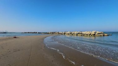 Adriyatik Denizi boyunca bir kış günü Rimini 'de boş bir plaj. Kaya dalgaları, berrak ve soğuk bir gökyüzünün altında suyun içinde duruyor. Yüksek kalite 4k görüntü