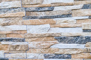 Görüntü, katmanlı, çok renkli taşlardan oluşan taş bir duvar sergiliyor, zengin ve dokulu bir görünüm yaratıyor. Yüksek kalite fotoğraf