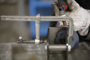 Bir atölye ortamındaki metal bir parçayı ölçmek için kalibreli kullanan yakın plan bir el çekimi, hassasiyet ve işçiliğe odaklanmış. Yüksek kalite fotoğraf