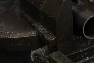 Metal bir boru, sağlam, koyu renkli mengeneye sıkıştırılır, endüstriyel ortamın altını çizer ve arka planı bulanıklaşır. Yüksek kalite fotoğraf