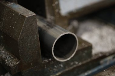 Metal bir boru, sağlam, koyu renkli mengeneye sıkıştırılır, endüstriyel ortamın altını çizer ve arka planı bulanıklaşır. Yüksek kalite fotoğraf