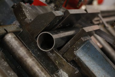 Metal bir boru, sağlam, koyu renkli mengeneye sıkıştırılır, endüstriyel ortamın altını çizer ve arka planı bulanıklaşır. Yüksek kalite fotoğraf