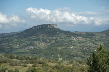 Dümdüz bir dağ olan Pietra di Bismantova 'nın uzak bir manzarası bulutlu bir gökyüzünün altındaki yuvarlanan tepelerin üzerinde belirgin bir şekilde duruyor ve manzaralı bir manzara sergiliyor. Reggio Emilia. Yüksek kalite fotoğraf