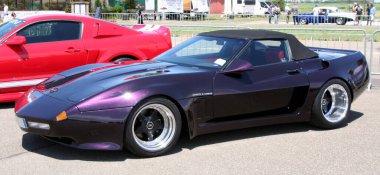 Carpi Modena, İtalya: 2009 07 06 Free Drag Race Etkinliği Bir araba fuarında park edilmiş mor Corvette, parlak tasarımı ve modifiye özellikleri ile arka planda kısmen görünür kırmızı bir araba ile sergilenmektedir. Yüksek kalite fotoğraf