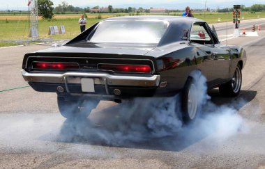 Carpi Modena, İtalya: 2009 07 06 Free Drag Race Etkinliği. Siyah klasik Dodge Charger yarış pistinde patlak bir performans sergiliyor, arka planda bulanık izleyiciler ile güç ve arka lastik dumanı sergiliyor. Yüksek kalite fotoğraf