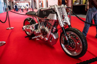 Modea, İtalya: 2025 03 Motor Festivali Fuarı Motosikleti siyah koltuklu ve metalik gümüş aksanlı modern, özel tasarlanmış bir motosiklet canlı kırmızı bir halının üzerinde sergilenmektedir. Arka planda insanlar görünüyor. Yüksek kalite pho