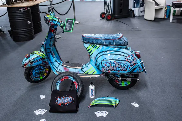 Modena, İtalya: 2025 03 Motor Festivali Fuarı Motosiklet A antika Vespa scooter 'ı. Renkli grafiti stili bir boya işi gri zeminde sergilenmektedir. Oyun kartları da dahil çeşitli aksesuarlar.