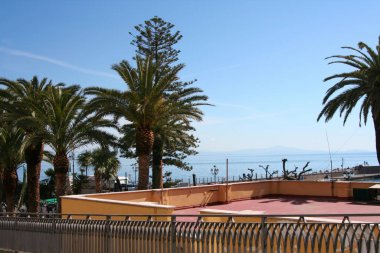 Pırıl pırıl palmiye ağaçları ve berrak gökyüzünün altındaki parlak mavi Akdeniz manzaralı bir gezinti alanı. Yüksek kalite fotoğraf