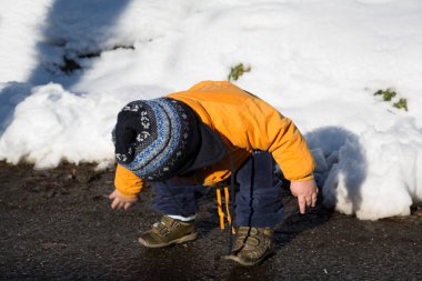 Sıcak turuncu bir ceket ve çizgili bir şapka giymiş sevimli bir çocuk karlı bir manzarada duruyor ve kış ortamını keşfediyor. Yüksek kalite fotoğraf