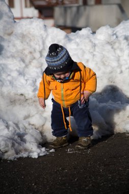 Sıcak turuncu bir ceket ve çizgili bir şapka giymiş sevimli bir çocuk karlı bir manzarada duruyor ve kış ortamını keşfediyor. Yüksek kalite fotoğraf