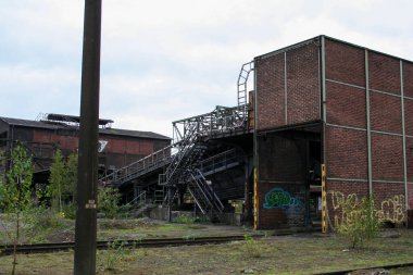Görünür pas, kırık yapılar ve renkli graffitilerle harap olmuş kırmızı tuğla sanayi binaları, bulutlu bir gökyüzünün altında, aşırı gelişmiş, terk edilmiş bir alanda geçiyor. Yüksek kalite fotoğraf
