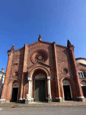 Büyük bir gül penceresi ve karmaşık mimari detayların yer aldığı tarihi bir kilisenin etkileyici kırmızı tuğla cephesi açık mavi gökyüzüne karşı kurulmuştur. Yüksek kalite fotoğraf