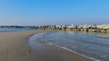 Kışın Rimini, Romagna Riviera 'da sakin bir sahilin geniş bir görüntüsü, kumlu kıyılar, sakin deniz, kayalık dalgalar ve berrak mavi bir gökyüzü, huzuru çağrıştırıyor. Yüksek kalite 4k görüntü