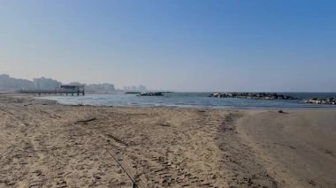 Kışın Rimini, Romagna Riviera 'da sakin bir sahilin geniş bir görüntüsü, kumlu kıyılar, sakin deniz, kayalık dalgalar ve berrak mavi bir gökyüzü, huzuru çağrıştırıyor. Yüksek kalite 4k görüntü