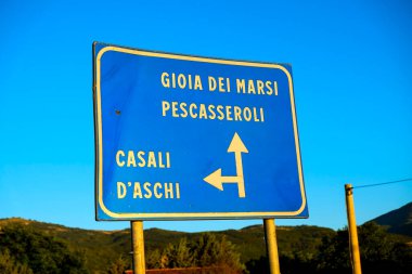 Sarı metin ve oklu açık mavi yol işareti Abruzzo 'da yaygın olan Gioia dei Marsi, Pescasseroli ve Casali d' Aschi gibi İtalyan kasabalarını gösteriyor. Yüksek kalite fotoğraf