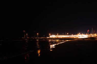 Geceleri Cesenatico plajı, kıyı şeridi otellerin ve işletmelerin uzak ışıklarını yansıtarak parlayan bir deniz manzarası yaratıyor. Yüksek kalite fotoğraf
