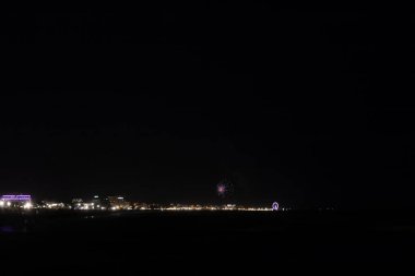Canlı bir havai fişek, kutlama gecesi boyunca İtalya 'nın Rimini kentinin aydınlık sahili ve sahili üzerindeki karanlık gökyüzünü aydınlatıyor. Yüksek kalite fotoğraf