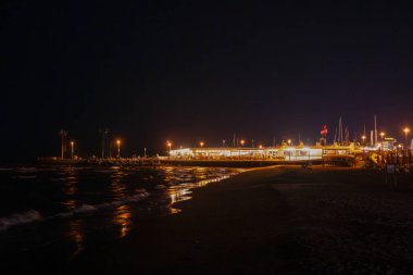 Geceleri Cesenatico plajı, kıyı şeridi otellerin ve işletmelerin uzak ışıklarını yansıtarak parlayan bir deniz manzarası yaratıyor. Yüksek kalite fotoğraf