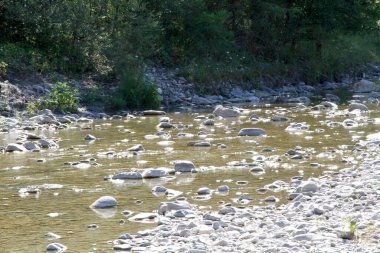 Güneş ışığı altında pürüzsüz, ıslak kayalardan oluşan bir yatağın üzerinden akan ışıl ışıl akan sığ bir nehrin yakın çekim, sepya tonlu görüntüsü. Yüksek kalite fotoğraf