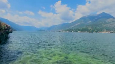 Como Gölü 'nün huzurlu manzarası. Arka planda dağ ve bulutlu bir gökyüzü. Ön planda dekoratif bir korkulukla çerçevelenmiş..