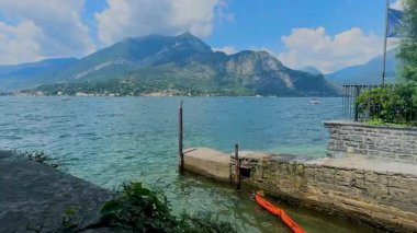Como Gölü 'nün, arka planında bir dağ ve bulutlu bir gökyüzü olan, taş bir duvar ve ön planda küçük bir rıhtım tarafından çerçevelenmiş resimli bir manzarası. Yüksek kalite 4k görüntü