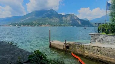 Como Gölü 'nün, arka planında bir dağ ve bulutlu bir gökyüzü olan, taş bir duvar ve ön planda küçük bir rıhtım tarafından çerçevelenmiş resimli bir manzarası. Yüksek kalite 4k görüntü