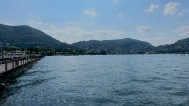 Bir sürat teknesi Como Gölü 'nün mavi sularında, yemyeşil dağlar ve güneşli bir gökyüzünün altındaki büyüleyici göl kentleri tarafından çerçevelenmiş beyaz bir uyanış yaratır. Yüksek kalite 4k görüntü