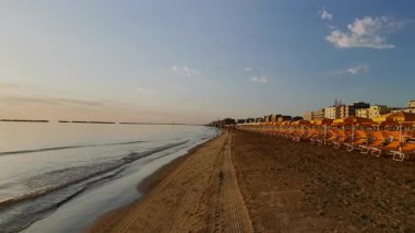 Gündoğumunda Cesenatico 'da düzenli dizilmiş şemsiyeleri ve güneşli yatakları olan geniş kumlu bir sahil. Yüksek kalite 4k görüntü