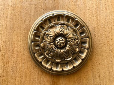 Ahşap bir yüzey üzerinde çiçek desenleri olan, karmaşık bir şekilde tasarlanmış eski pirinç kapı tokmağının yakın plan ayrıntıları, zanaatkarlık sergiliyor. Yüksek kalite fotoğraf