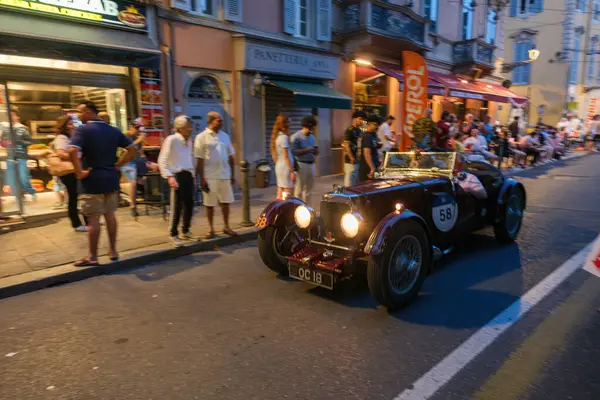 Parma, İtalya: 2025 06 20 Mille Miglia klasik rali klasik araba yarışı, klasik mavi bir yarış arabası açık hava kafesinde yemek yiyen insanlarla dolu bir caddede ilerliyor. Yüksek kalite fotoğraf