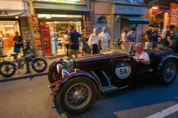 Parma, İtalya: 2025 06 20 Mille Miglia klasik rali klasik araba yarışı, klasik mavi bir yarış arabası açık hava kafesinde yemek yiyen insanlarla dolu bir caddede ilerliyor. Yüksek kalite fotoğraf