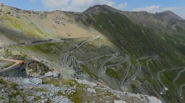 Ünlü Stelvio Geçidi 'nin dolambaçlı dağ yollarının panoramik bir görüntüsü. Görkemli tepelerin ve bulutlu gökyüzünün zeminine kurulmuş..