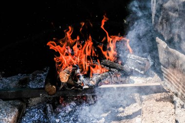 Parlak turuncu alevler ve yanan odunlardan yükselen parlayan közler dumanlı ve karanlık çevreli, kırsal bir ateş deliğinde. Yüksek kalite fotoğraf