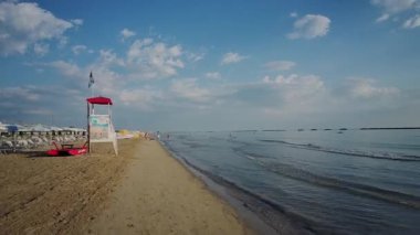 İnsanlar güzel bir öğleden sonra Cesenatico 'da kumlu bir plajda yürüyüp dinleniyorlar. Güneş ılık bir parıltıyla suyun üzerinde batıyor. Yüksek kalite 4k görüntü