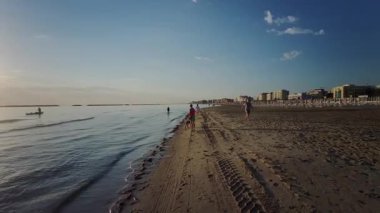 İnsanlar güzel bir öğleden sonra Cesenatico 'da kumlu bir plajda yürüyüp dinleniyorlar. Güneş ılık bir parıltıyla suyun üzerinde batıyor. Yüksek kalite 4k görüntü