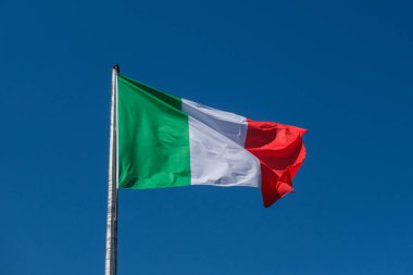 İtalyan üç renkli bayrağı, yeşil, beyaz ve kırmızı çizgileriyle rüzgarda zarif bir şekilde dalgalanır açık mavi gökyüzüne karşı. Yüksek kalite fotoğraf