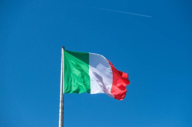 İtalyan üç renkli bayrağı, yeşil, beyaz ve kırmızı çizgileriyle rüzgarda zarif bir şekilde dalgalanır açık mavi gökyüzüne karşı. Yüksek kalite fotoğraf